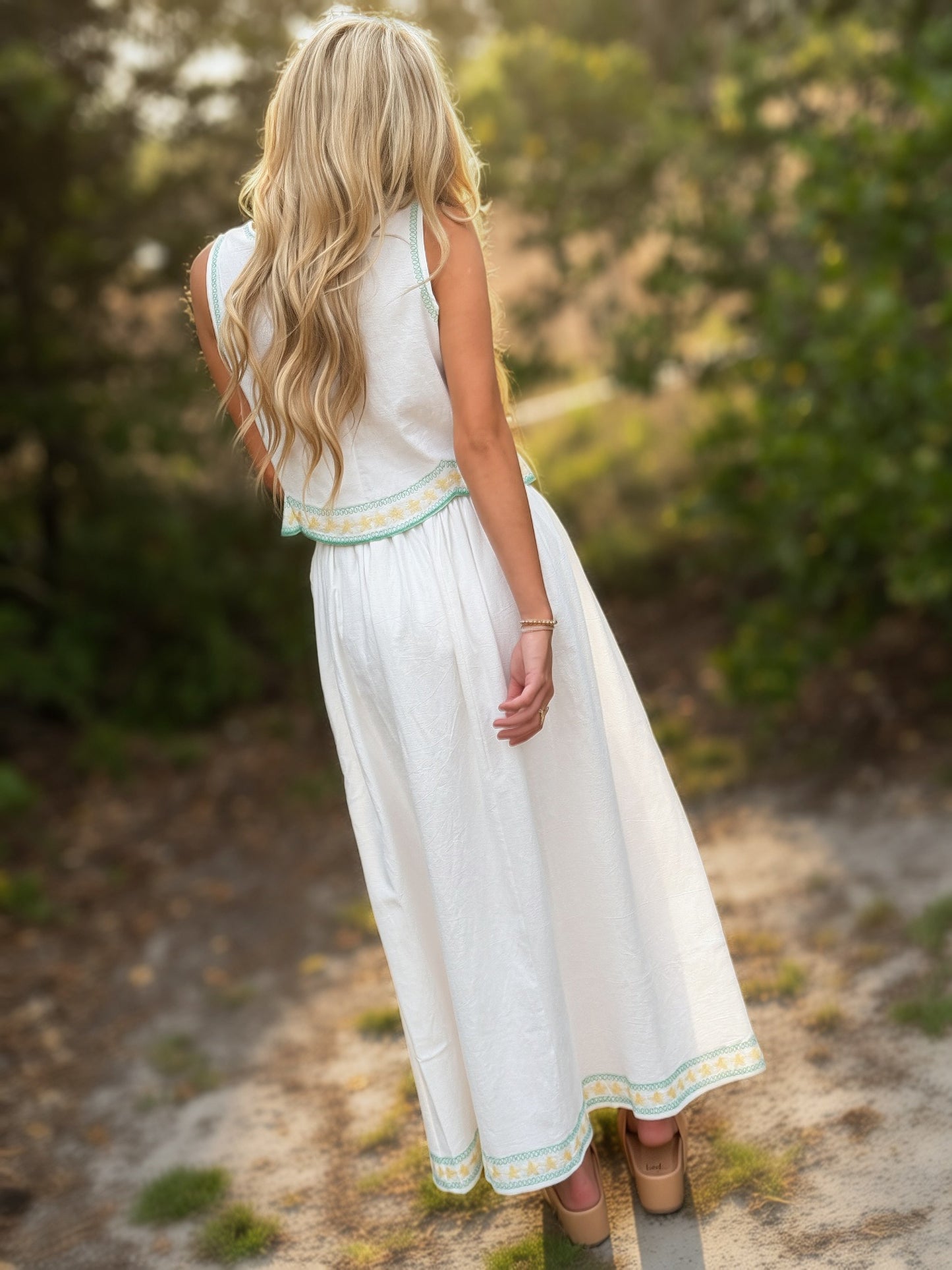 Woman in a white dress with green trim standing in a natural setting