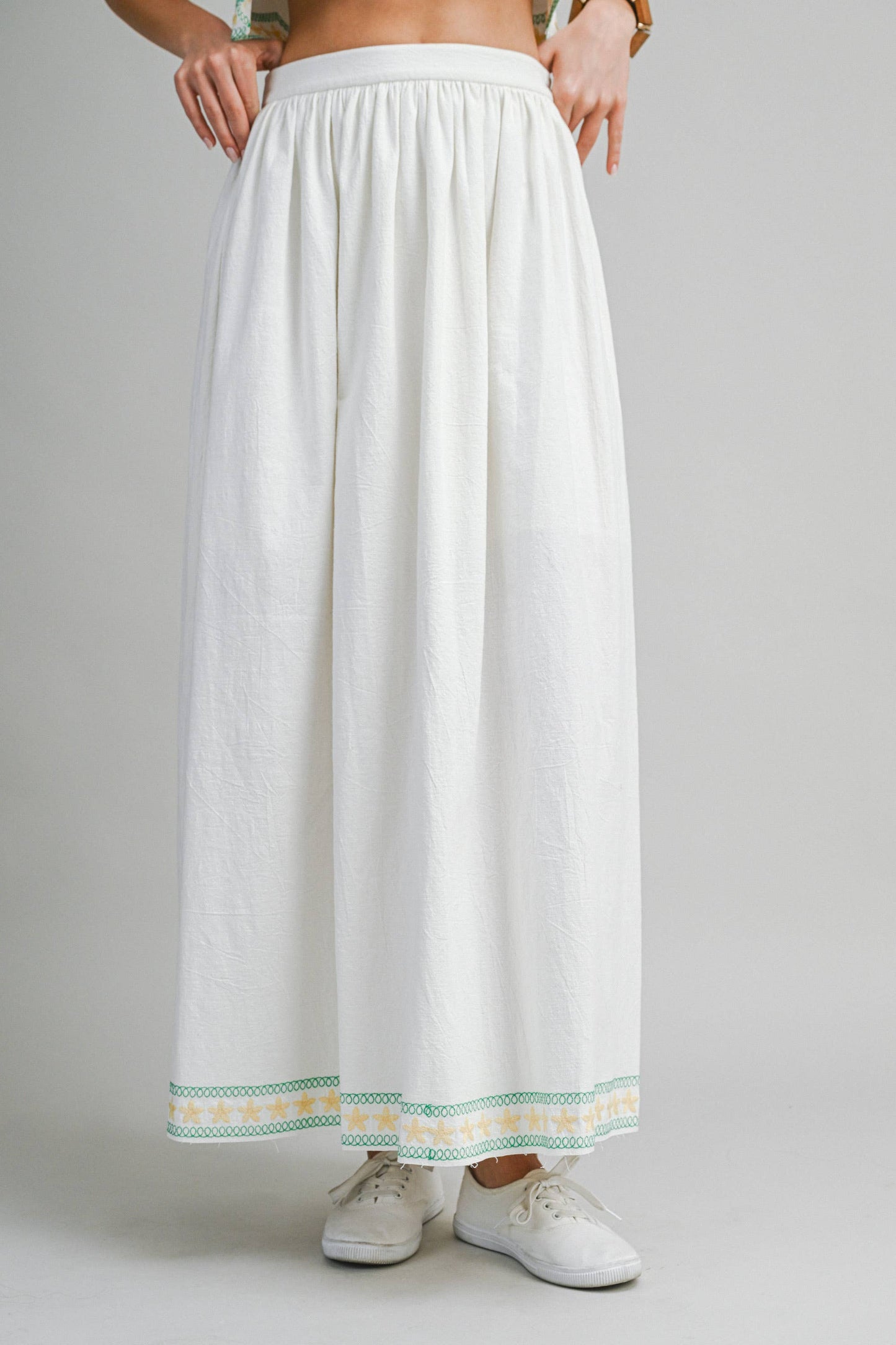White skirt with green and yellow trim worn by a person on a gray background