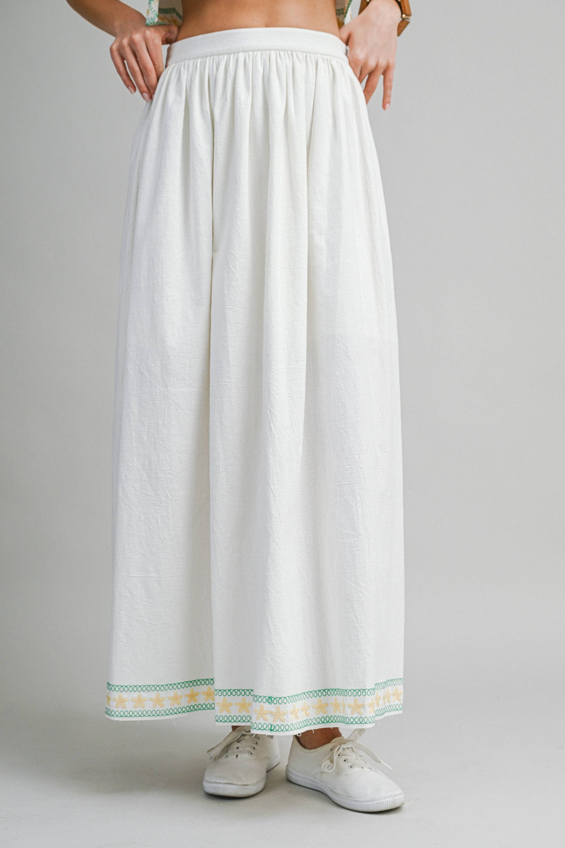 White skirt with green and yellow trim worn by a person on a gray background