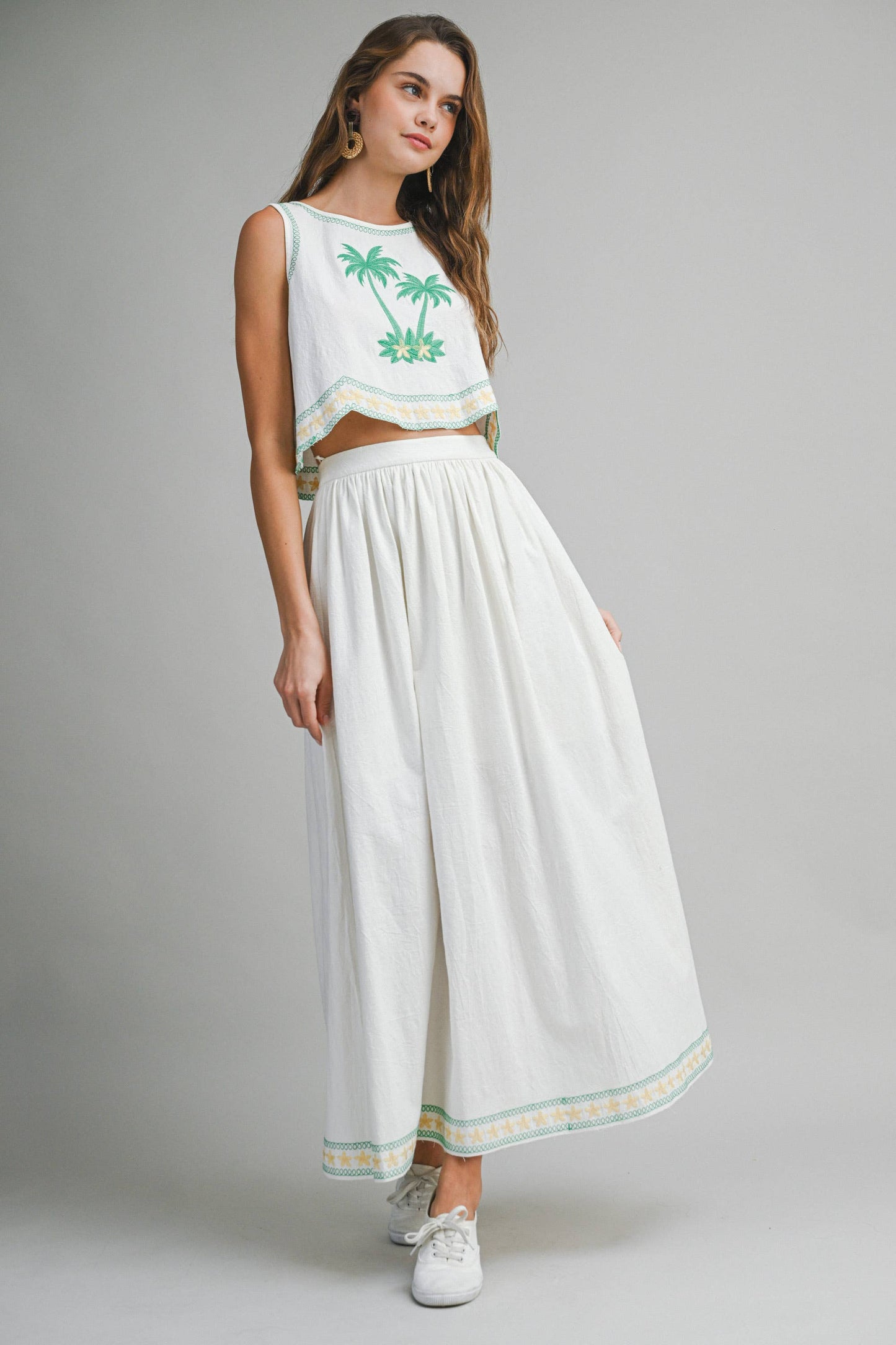 Woman wearing a white outfit with green embroidery on a gray background