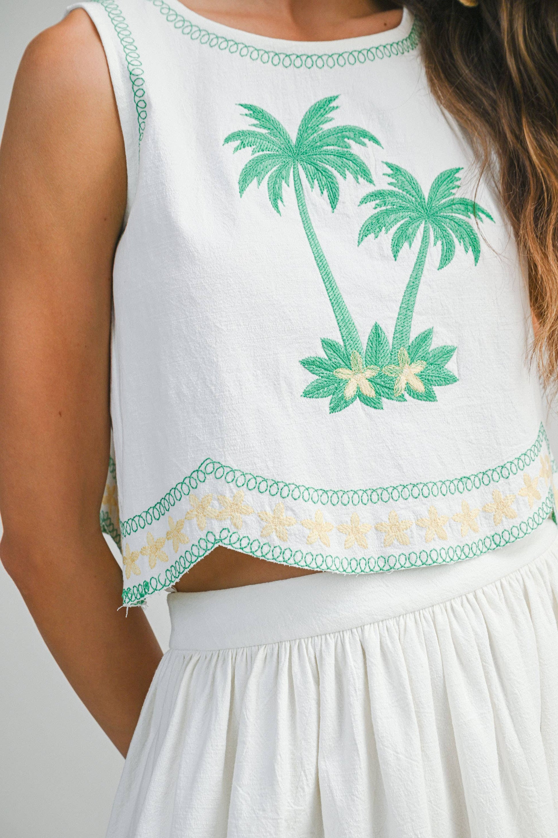 White sleeveless top with green palm tree embroidery on a plain background