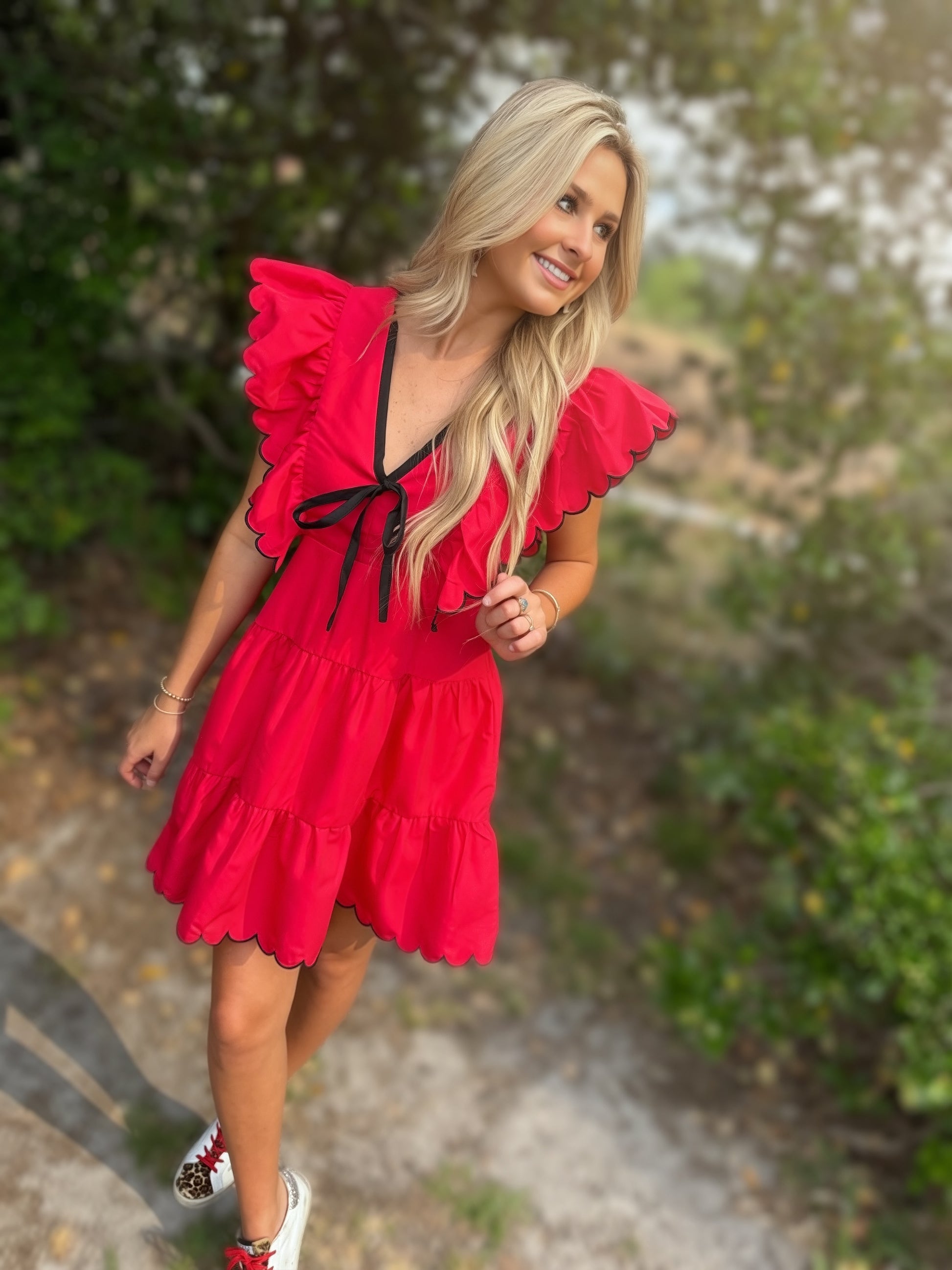 Woman wearing a red dress with ruffled sleeves and black trim, standing outdoors.