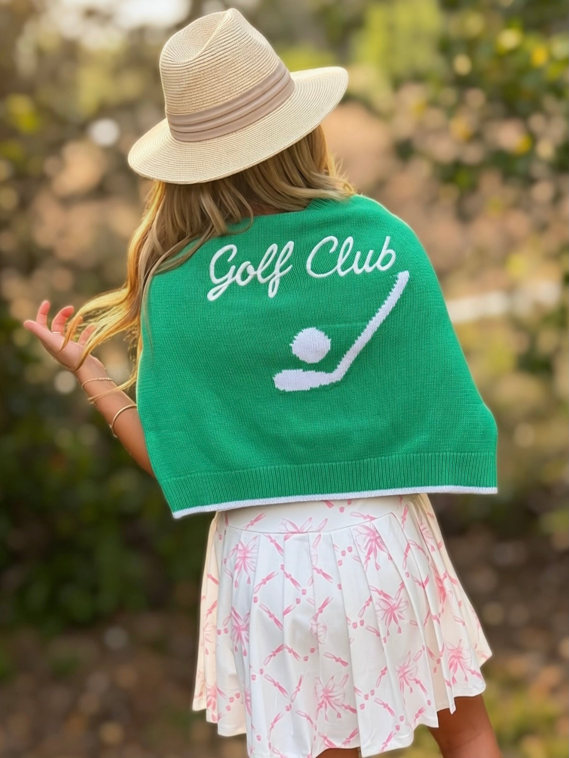Person wearing a green 'Golf Club' jacket with a hat, standing outdoors.
