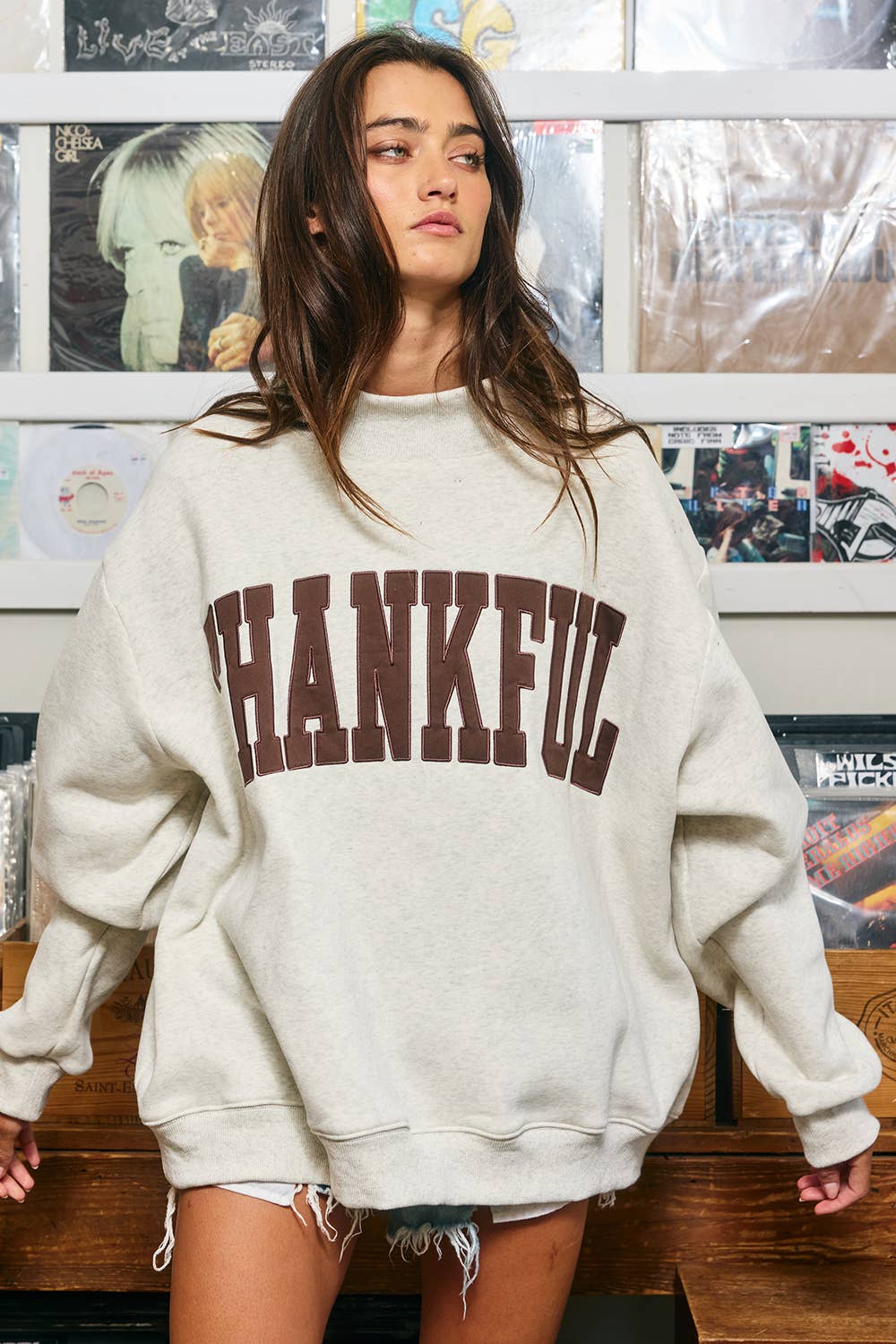 Model wearing a light heathered oversized mock neck sweatshirt with brown THANKFUL appliqué lettering, dropped shoulders, and ribbed trim.