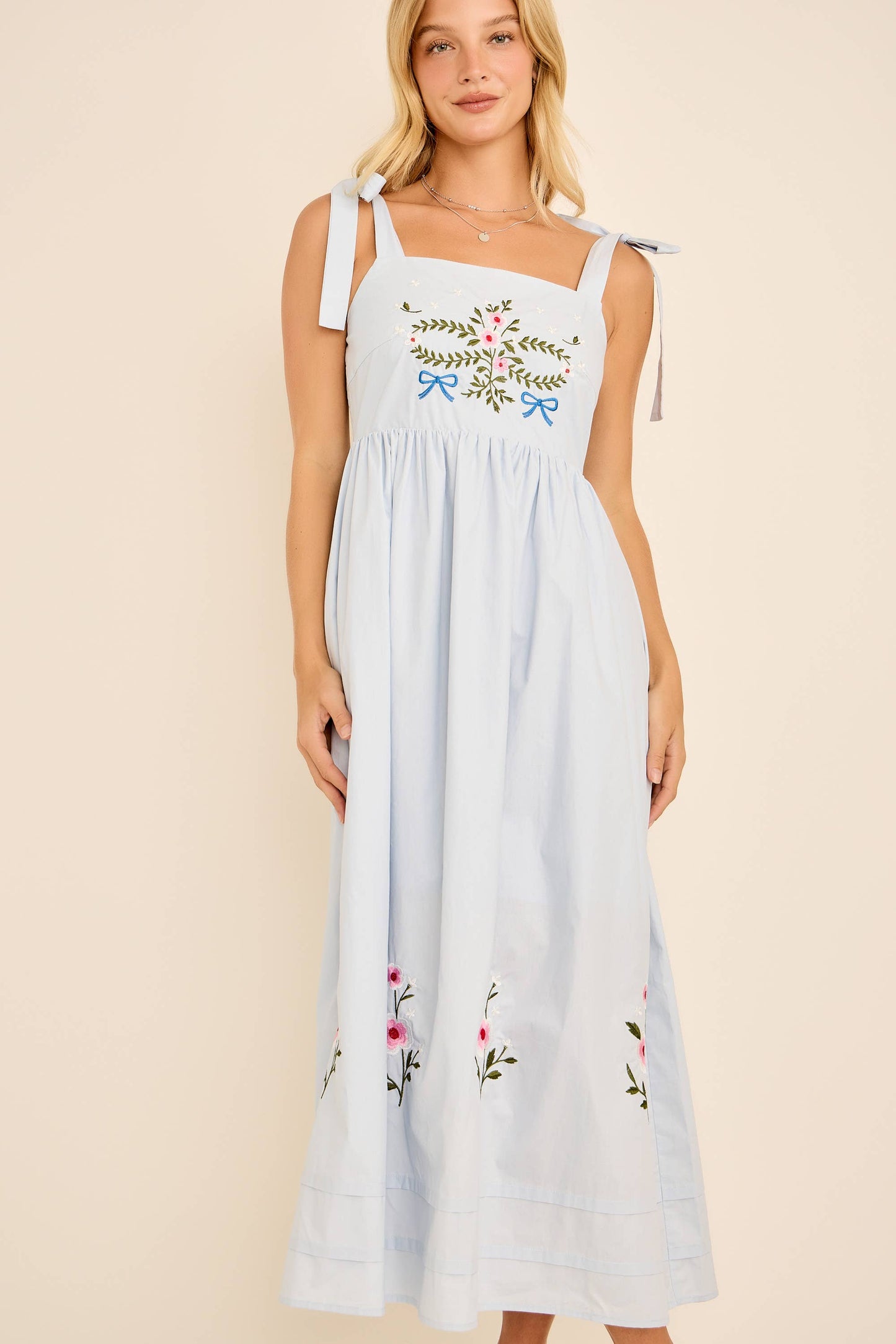 Woman wearing a light blue dress with floral embroidery on a beige background