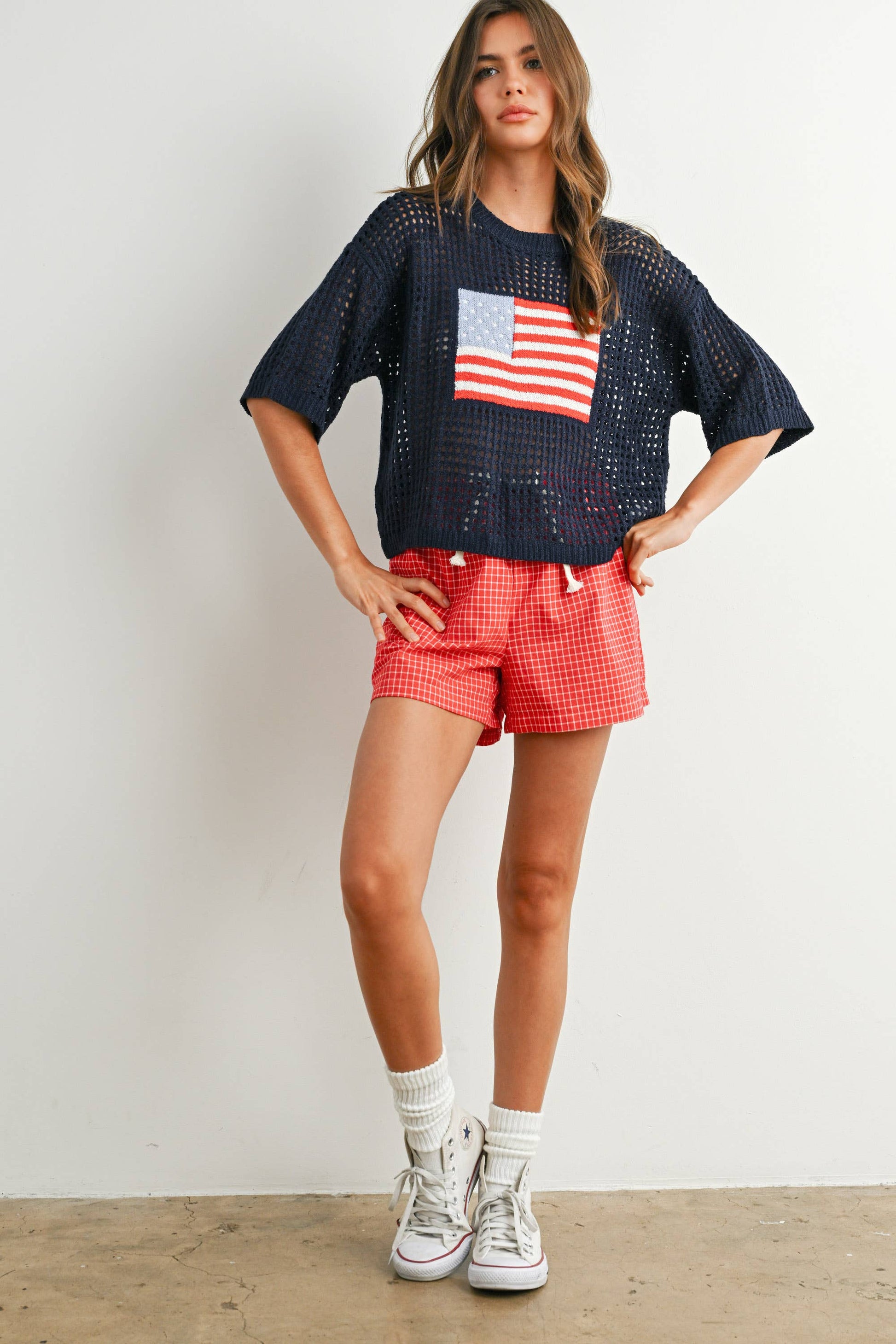 Woman wearing a navy blue top with an American flag design and red shorts against a white background