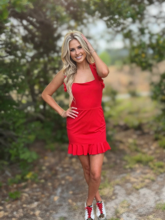 Woman in a red dress standing outdoors with greenery in the background